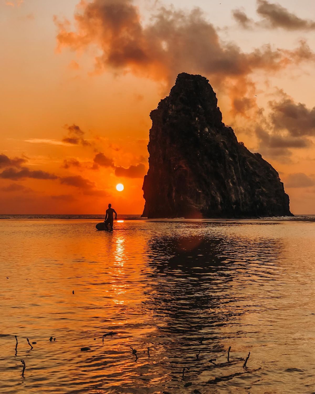 Pôr do sol alaranjado refletido no mar com formação rochosa em Fernando de Noronha